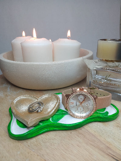 Rose gold watch on a decorative stand with candles and a heart-shaped box.