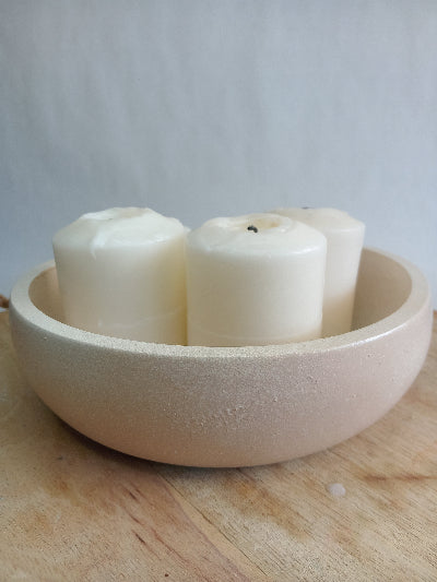 Beige concrete bowl with candles inside on a wooden surface.