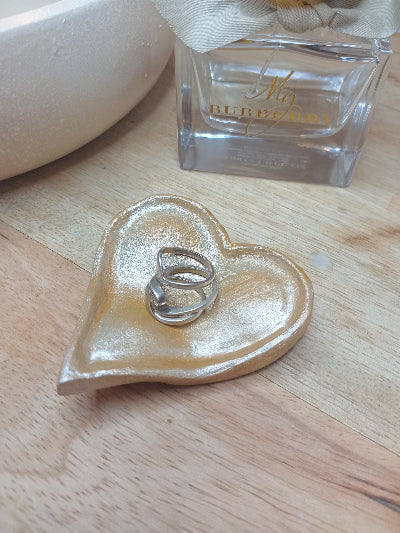 Heart-shaped dish with rings on a wooden surface next to a bottle of perfume.