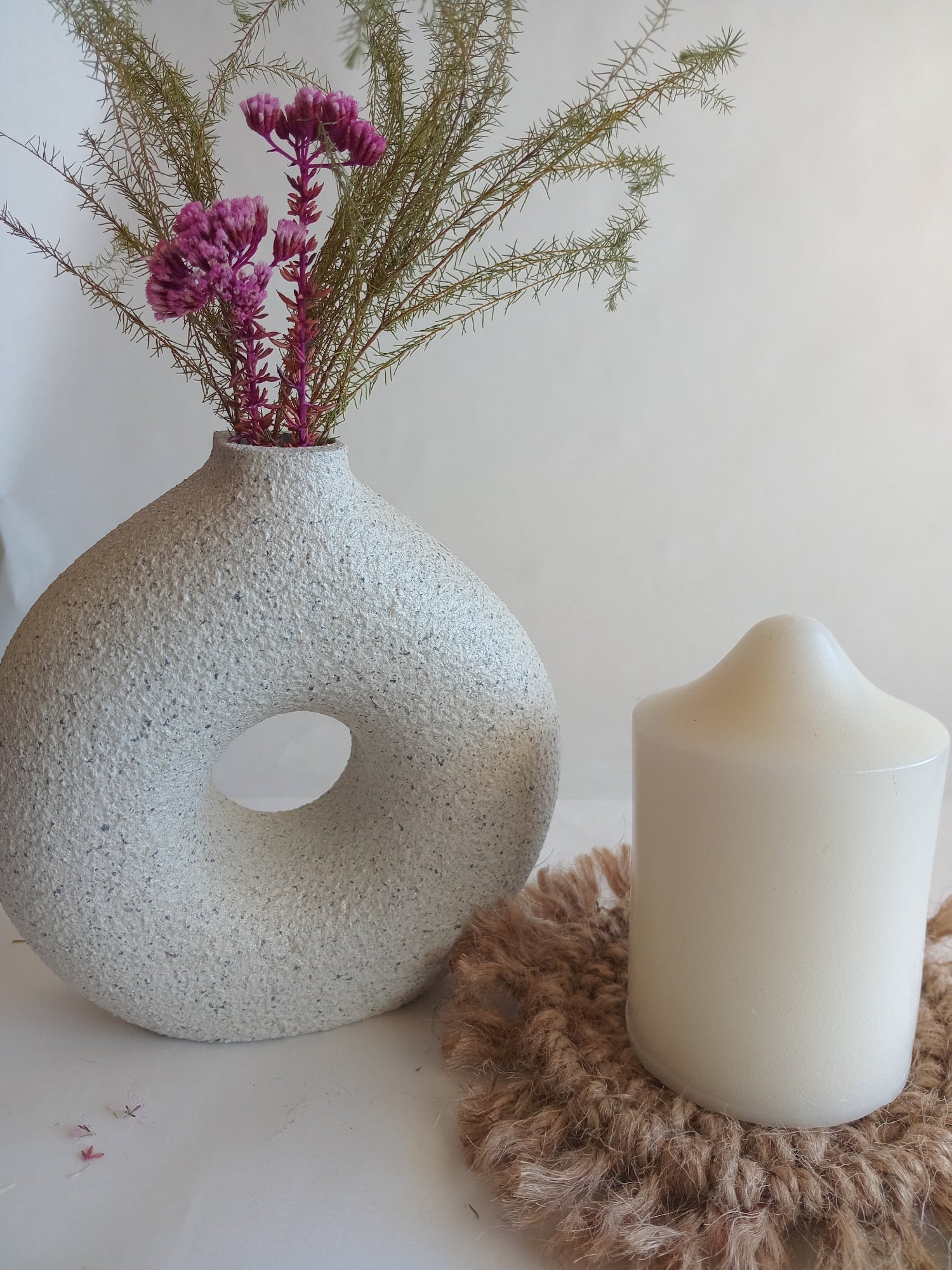 Textured vase with flowers, candle, and decorative item on a light background