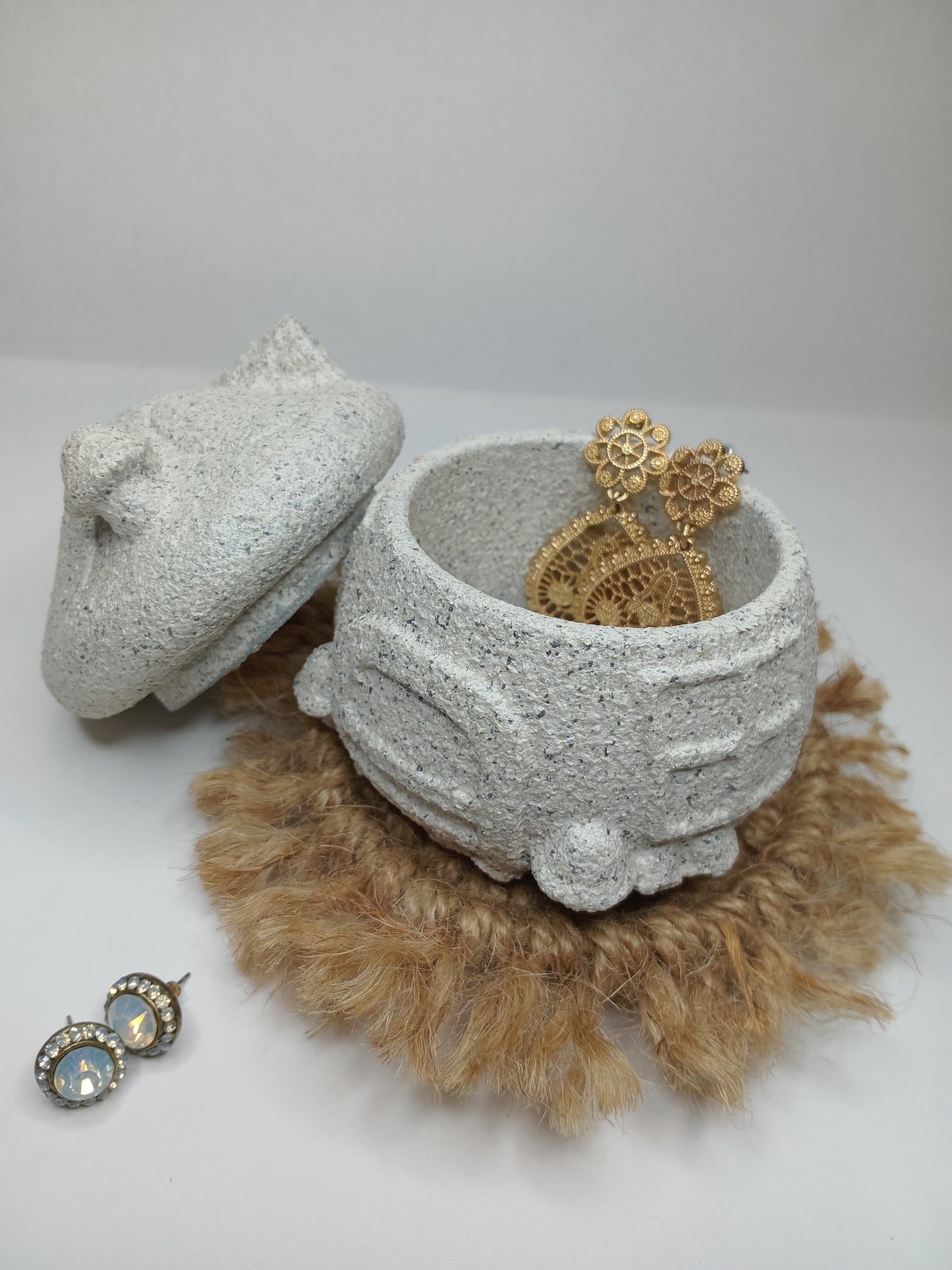 Decorative stone trinket mushroom house with gold earings and beige decorative item on a white background