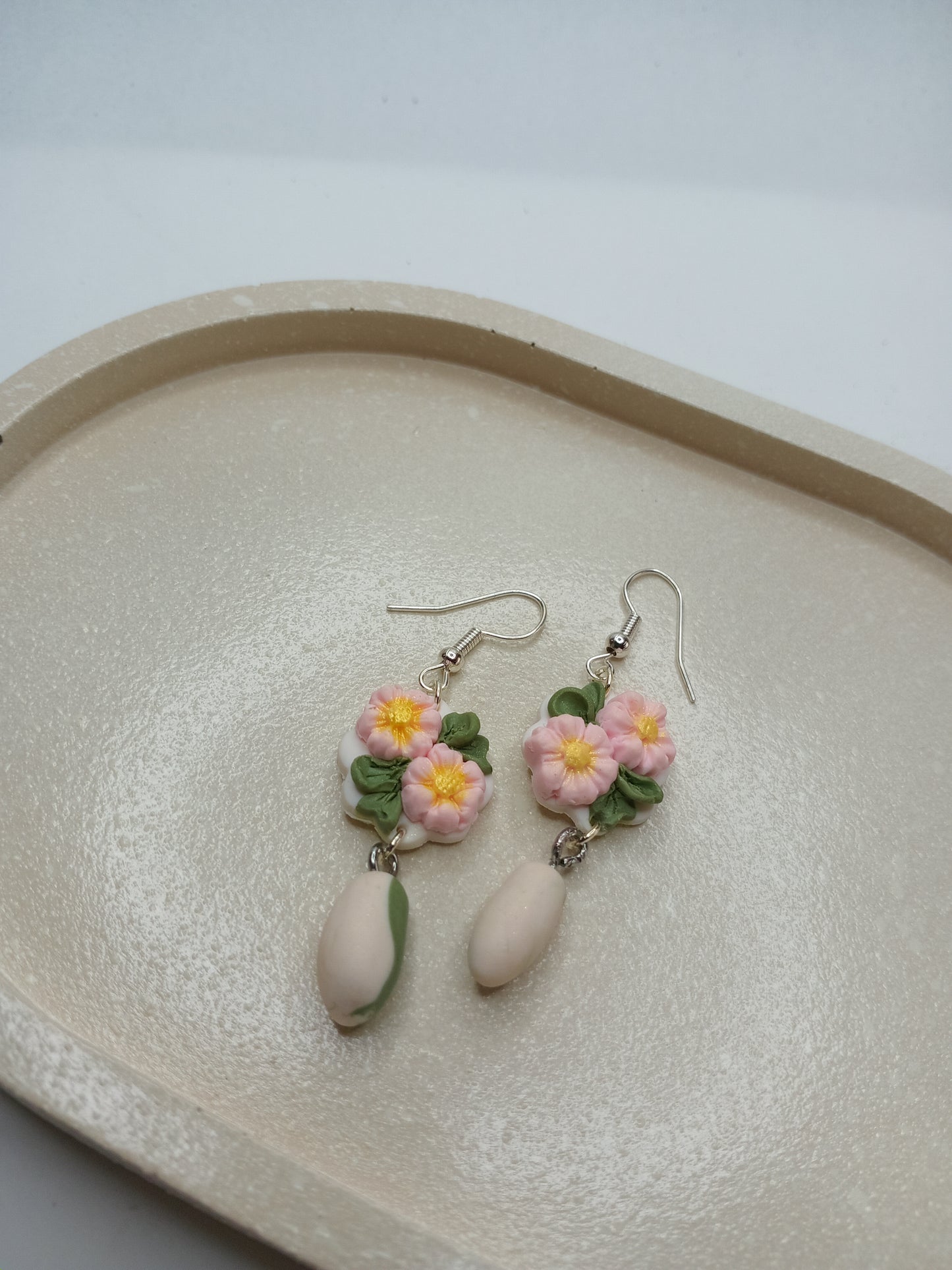 Floral earrings on a textured beige trinket dish with a white background