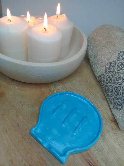 Blue clay shell shaped soap dish with candles and a face towel alongside it.