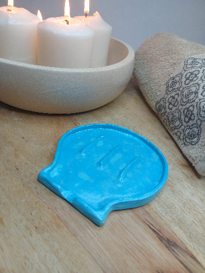 Blue clay shell shaped soap dish with candles and a face towel alongside it.