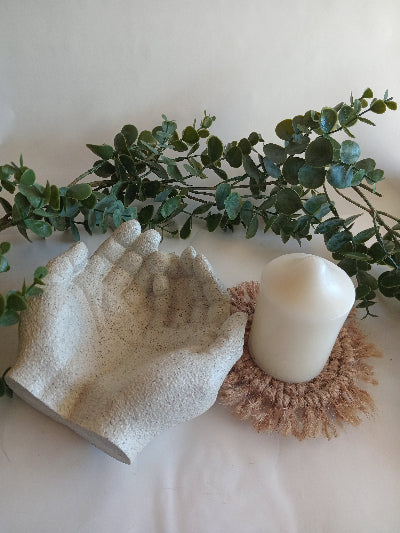 Decorative stone textured giving hands with a candle on a macrame coaster with some greenery around.