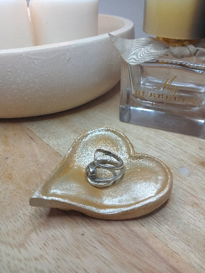 Heart-shaped dish with a ring on a wooden surface next to a perfume bottle.