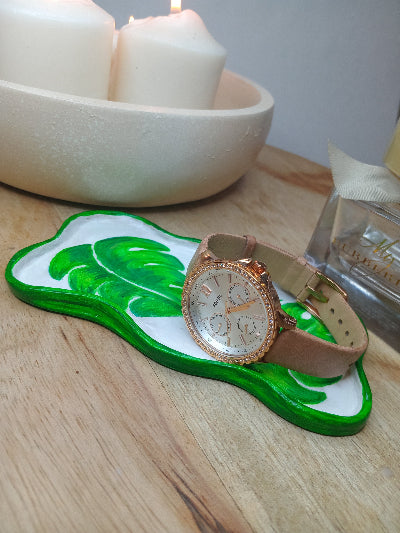 Rose gold watch on a Green monstera leafed clay trinket tray on a wooden board with candles