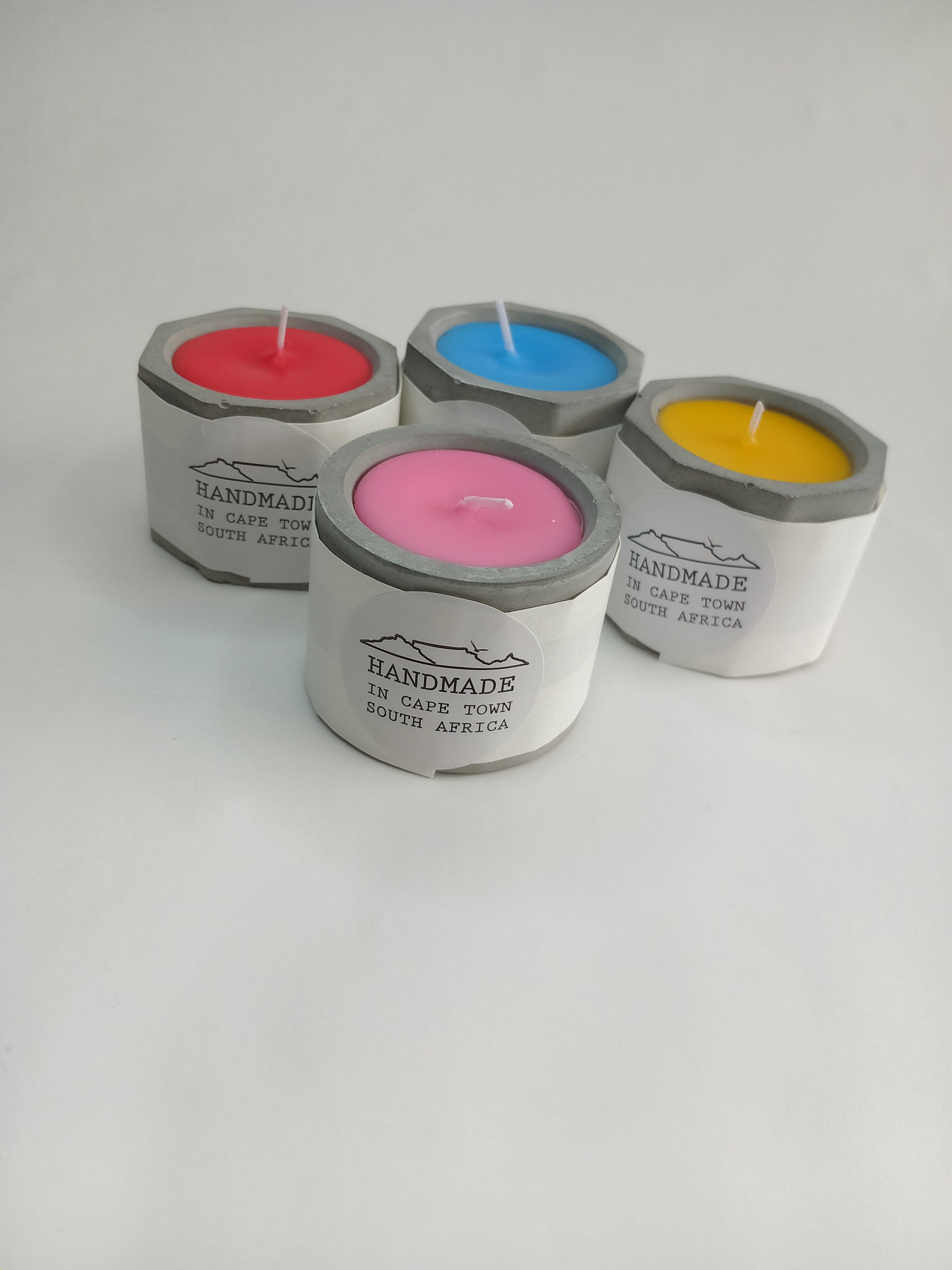 Four colorful candles in concrete casted holders on a white background