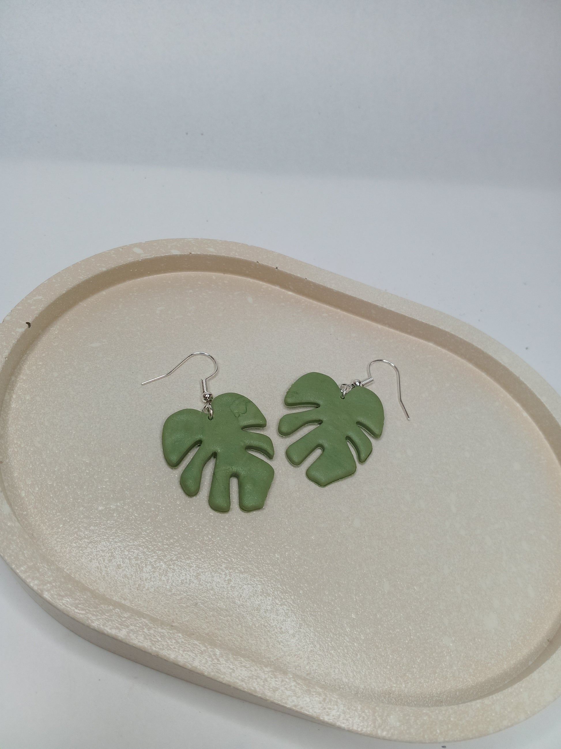 Green leaf-shaped earrings on a beige oval trinket dish against a white background