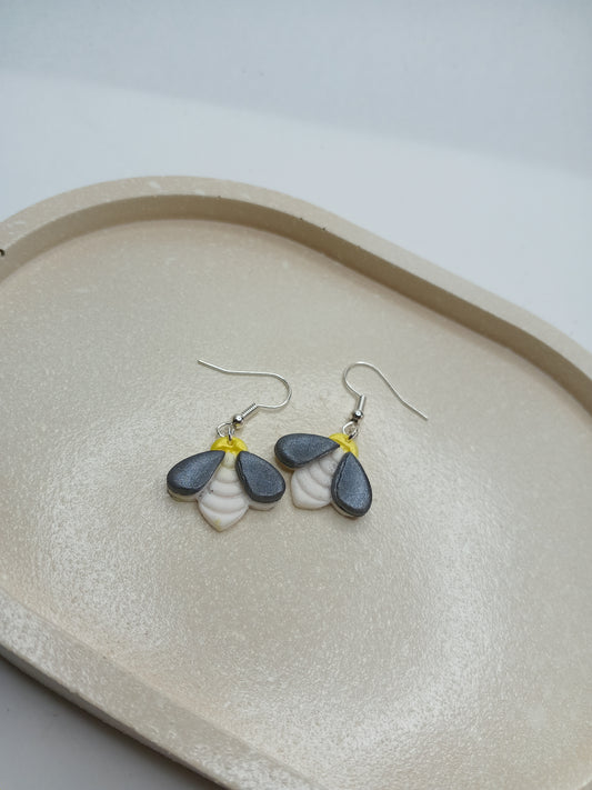 Pair of bee shaped earrings on a beige trinket dish with a white background