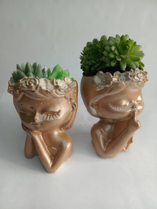 Two soft gold metallic planter sculptures of women with succulents on a light gray background